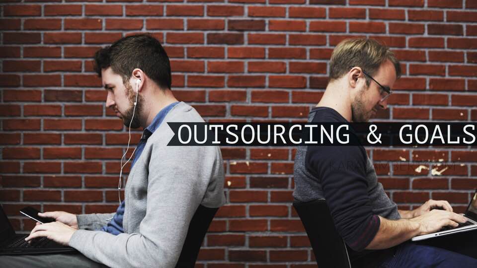 Two men sitting in front of a brick wall discussing outsourcing strategies.